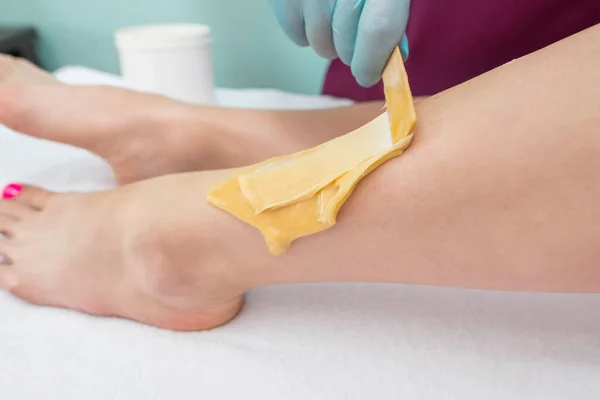 leg sugaring. A beautician makes a sugar paste depilation of a woman's legs in a beauty salon. Female aesthetic cosmetology. Apply sugar paste with a wooden spatula.