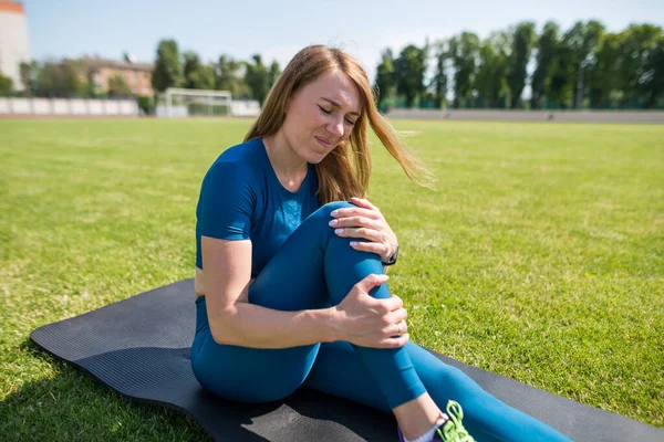 Sports injury of the knee. A woman experiences pain in her knee while exercising at a sports stadium. healthcare concept.