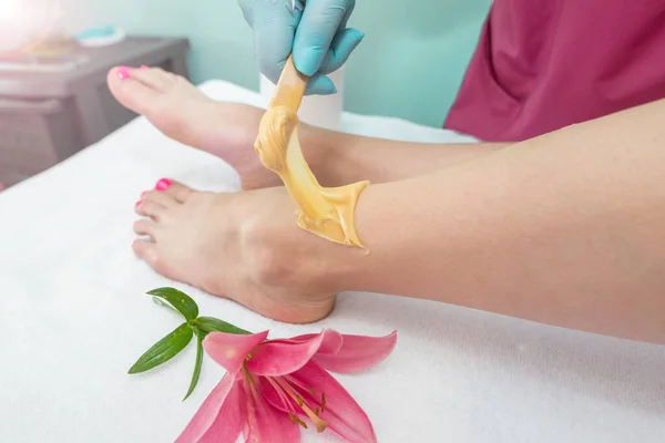 leg sugaring. A beautician makes a sugar paste depilation of a woman\'s legs in a beauty salon. Female aesthetic cosmetology. Apply sugar paste with a wooden spatula.