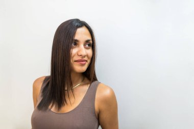 Close-up of a beautiful sexy brunette with a big bust on a white background. An attractive young woman in a tight tank top poses for the camera.