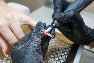 Close-up of a woman in a nail salon getting a manicure in a beauty salon from a beautician who uses an electric nail polish remover machine with flying shards all around. The concept of technology, nail care.