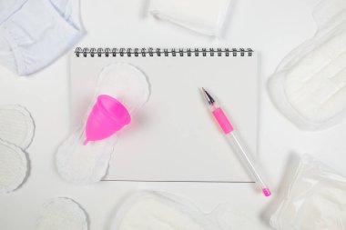 notepad with pen pads menstrual cup and panties on white. copy space, place for text. The concept of menstruation, women's creative days.