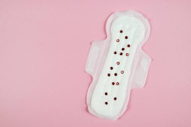 Photo of a sanitary pad with red confetti on an isolated pastel pink background with copy space, top view