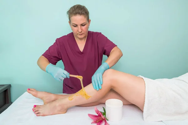 leg sugaring. A beautician makes a sugar paste depilation of a woman\'s legs in a beauty salon. Female aesthetic cosmetology. Apply sugar paste with a wooden spatula.