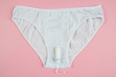 Top view of white panties and tampon on pastel pink background.