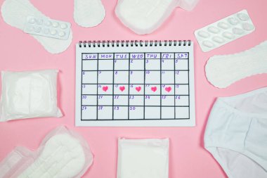 Top view photo of red heart marks on calendar, panty,sanitary pads on isolated pastel pink background