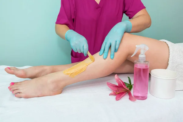 leg sugaring. A beautician makes a sugar paste depilation of a woman\'s legs in a beauty salon. Female aesthetic cosmetology. Apply sugar paste with a wooden spatula.