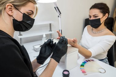 The manicurist covers the client's nails with red varnish. Manicure in a beauty salon. Nail care concept.