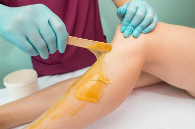 Woman undergoing leg hair removal procedure with sugaring paste in salon. Skin care, remove hair with sugar paste