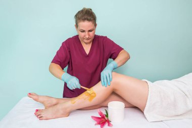 leg sugaring. A beautician makes a sugar paste depilation of a woman's legs in a beauty salon. Female aesthetic cosmetology. Apply sugar paste with a wooden spatula.