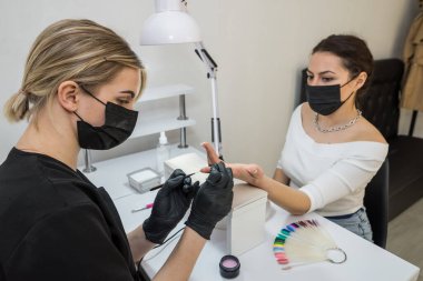 The manicurist covers the client's nails with red varnish. Manicure in a beauty salon. Nail care concept.