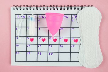Top view of photo of female calendar marks, sanitary napkins and tampons on pastel pink background