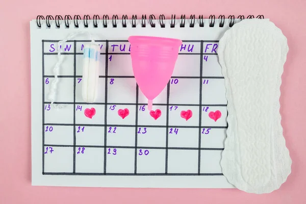 Top view of photo of female calendar marks, sanitary napkins and tampons on pastel pink background