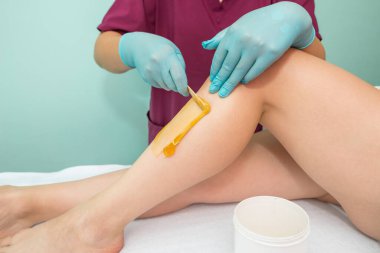 Woman undergoing leg hair removal procedure with sugaring paste in salon. Skin care, remove hair with sugar paste