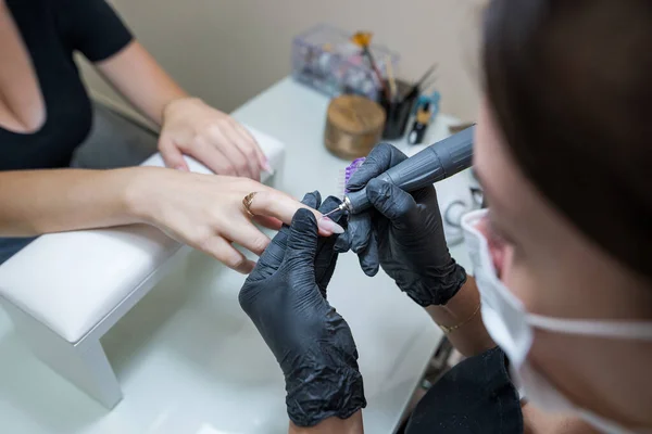 Beauty salon, manicure. Professional hardware manicure using an electric machine in a beauty salon. the master uses an electric machine to remove the cuticle