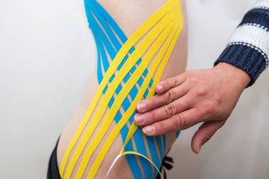 Fizyoterapist, genç yetişkin bir kadının muayenehanesindeki karın bölgesine yapışkan elastik tedavi bandı uyguluyor. Yaralı Rehabilitasyon ve Sağlık Hizmetleri