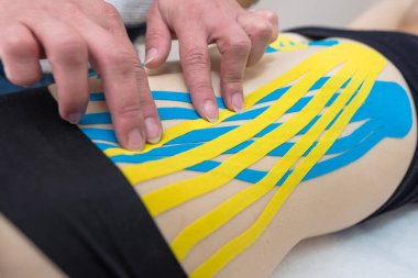 Kadın bir fizyoterapistin elleri, bir doktorun ofisindeki kanepede yatan genç, ince, atletik bir kadının karın kaslarına yapışkan elastik tedavi bandı uyguluyor. Yaralı Rehabilitasyon ve Sağlık Hizmetleri