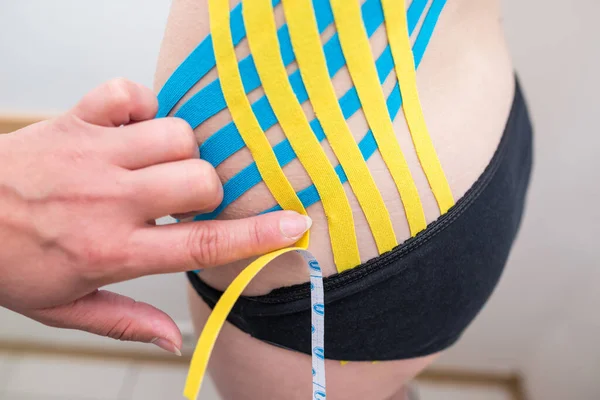 physiotherapist applying adhesive elastic therapeutic tape to the side of the abdomen of a young adult athletic woman in a doctor\'s office. Injury Rehabilitation and Healthcare