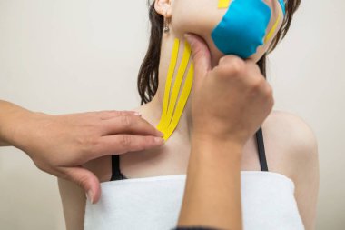 Kinesio kayıt yapıyor. Fizyoterapist hastanın boynuna kineziyoloji bandı yapıştırıyor. Travma sonrası rehabilitasyon, spor fizyoterapisi, boyun sıkma..