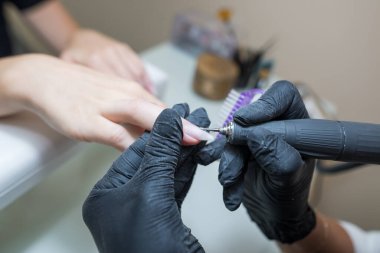Güzellik salonu, manikür. Güzellik salonunda elektrikli makine kullanan profesyonel donanım manikürü. Üstat tırnak derisini sökmek için elektrikli makine kullanıyor.