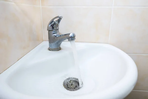 Tap with drinking water in the bathroom.School\'s bathroom water faucets with tap water running strong, selective focus on the closest faucet with shallow depth of field