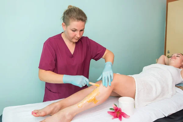 leg sugaring. A beautician makes a sugar paste depilation of a woman\'s legs in a beauty salon. Female aesthetic cosmetology. Apply sugar paste with a wooden spatula.