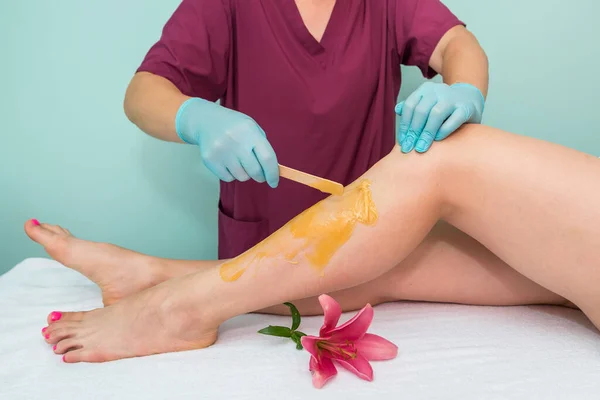 leg sugaring. A beautician makes a sugar paste depilation of a woman\'s legs in a beauty salon. Female aesthetic cosmetology. Apply sugar paste with a wooden spatula.