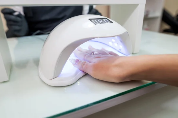 female hand with manicured nails inside a UV lamp in a nail salon