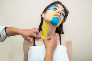 Kinesio kayıt yapıyor. Fizyoterapist hastanın boynuna kineziyoloji bandı yapıştırıyor. Travma sonrası rehabilitasyon, spor fizyoterapisi, boyun sıkma..