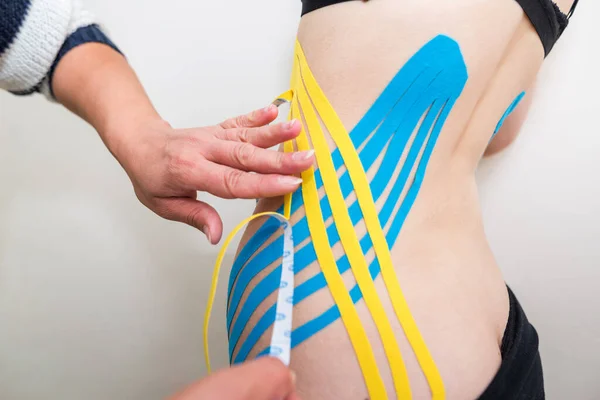physiotherapist applying adhesive elastic therapeutic tape to the side of the abdomen of a young adult athletic woman in a doctor\'s office. Injury Rehabilitation and Healthcare