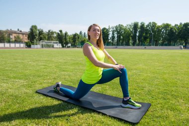 Spor yapan atletik bir kadın spor yapıyor. Şehir stadyumunun çimlerinde antrenman, ısınma..