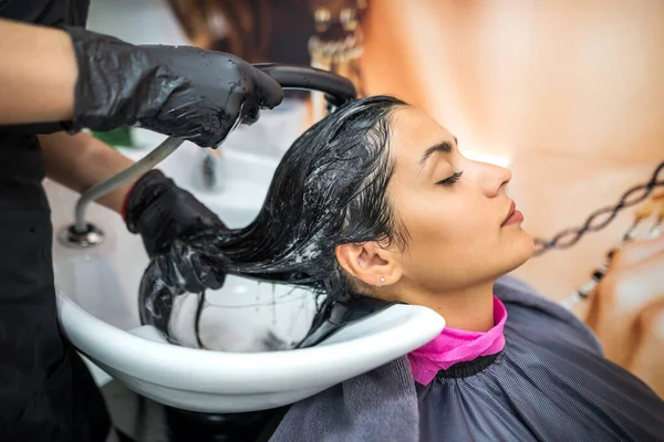 female client washes hair in salon, professional hairdresser washes head of female client with water and shampoo treatment, hairstyle beauty hair care, fashion service.