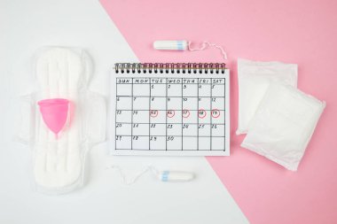 Kırmızı takvim işaretleri, regl kupası, izole edilmiş beyaz ve pastel pembe arka planda hijyenik pedler ve tamponlar..