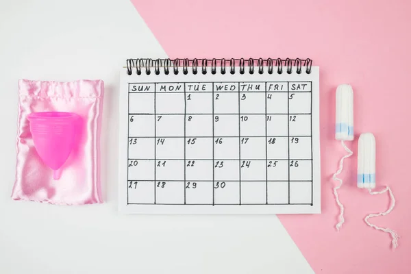 Top view of the calendar of women\'s critical days with pads and accessories on a white and pink background. The concept of women\'s periods.