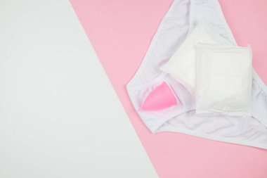 Pembe ve beyaz arkaplanlı külot pedleri ve regl kupası fotokopi alanı, üst görünüm