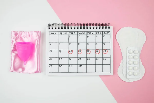 Top view of the calendar of women\'s critical days with pads and accessories on a white and pink background. The concept of women\'s periods.