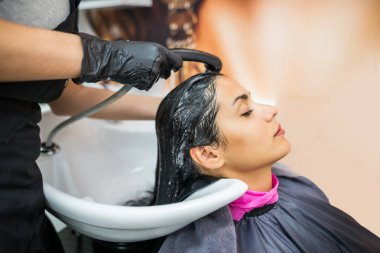 female client washes hair in salon, professional hairdresser washes head of female client with water and shampoo treatment, hairstyle beauty hair care, fashion service.