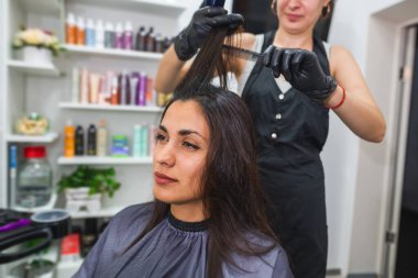 Güzellik salonunda saç bakımı, sandalyede oturan bir kadın saçlarıyla ilgili prosedürler yapıyor. Saç keratin işlemi. Maske, düzleştirme, kadın saçı katmanı