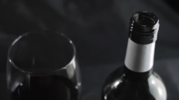 Bir bardak kırmızı şarap ve siyah bir arka planda bir şişe. Yavaş çekim — Stok video