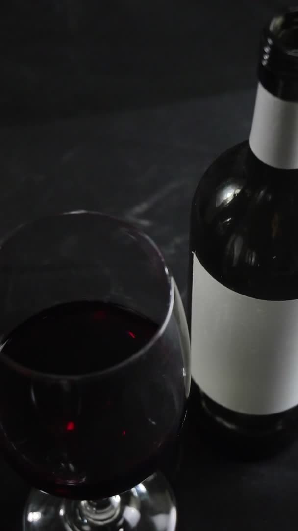 Склянка червоного вина і пляшка на темному фоні. Повільний рух — стокове відео