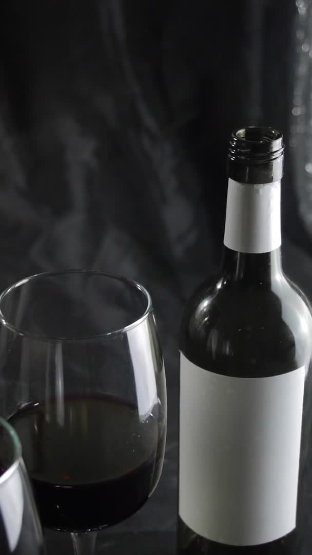 Glas rode wijn en een fles op een donkere achtergrond. Langzame beweging — Stockvideo