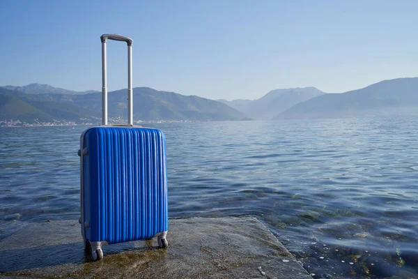 Μπλε βαλίτσα στο φόντο της θάλασσας και των βουνών — Φωτογραφία Αρχείου