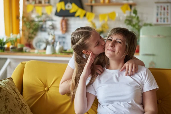 Fille embrasse maman assise sur le canapé dans la cuisine Images De Stock Libres De Droits