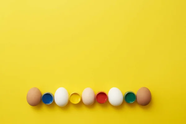 Chicken eggs and paints on a yellow background for easter — Stock Photo, Image