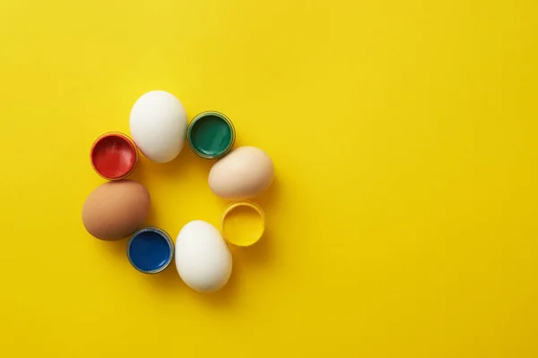 Chicken eggs and paints on a yellow background for colorful easter — Stock Photo, Image