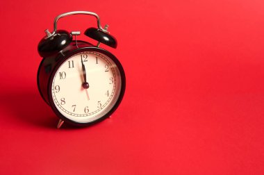Gece yarısı suratlı siyah bir çalar saat. Gece yarısı oldu. Noel ve Yeni Yıl kutlamaları kavramı kırmızı arkaplanda izole edilmiş ve reklam için fotokopi alanı var.