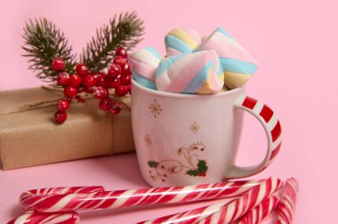 Renkli marşmelovlu kahve fincanı, el işi kağıdında noel hediyesi, pembe pastel arka planda kutsal ve çizgili şeker kamışı. Kopya alanı ile Noel ve Yeni Yıl kavramı