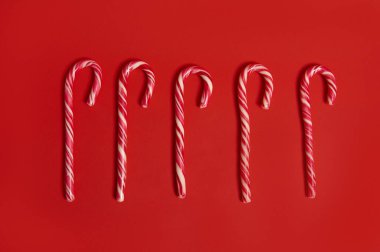 Yüksek açılı Noel dekorasyonu manzarası. Beş tane şeker kamışı, kırmızı arka planda duran noel lolipopları ve reklam için fotokopi alanı olan düz bir kompozisyon.