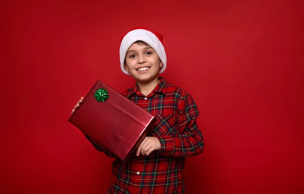 Schöner Junge Mit Nikolausmütze Und Kariertem Hemd Hält Weihnachtsgeschenk Glitzerndem — Stockfoto
