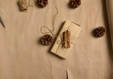 Kahverengi el sanatları hediye kağıdına sarılı bir Noel hediyesinin düz kompozisyonu. İple sarılı bir fiyonk. Noel ağacı konilerinin yanında duruyor.